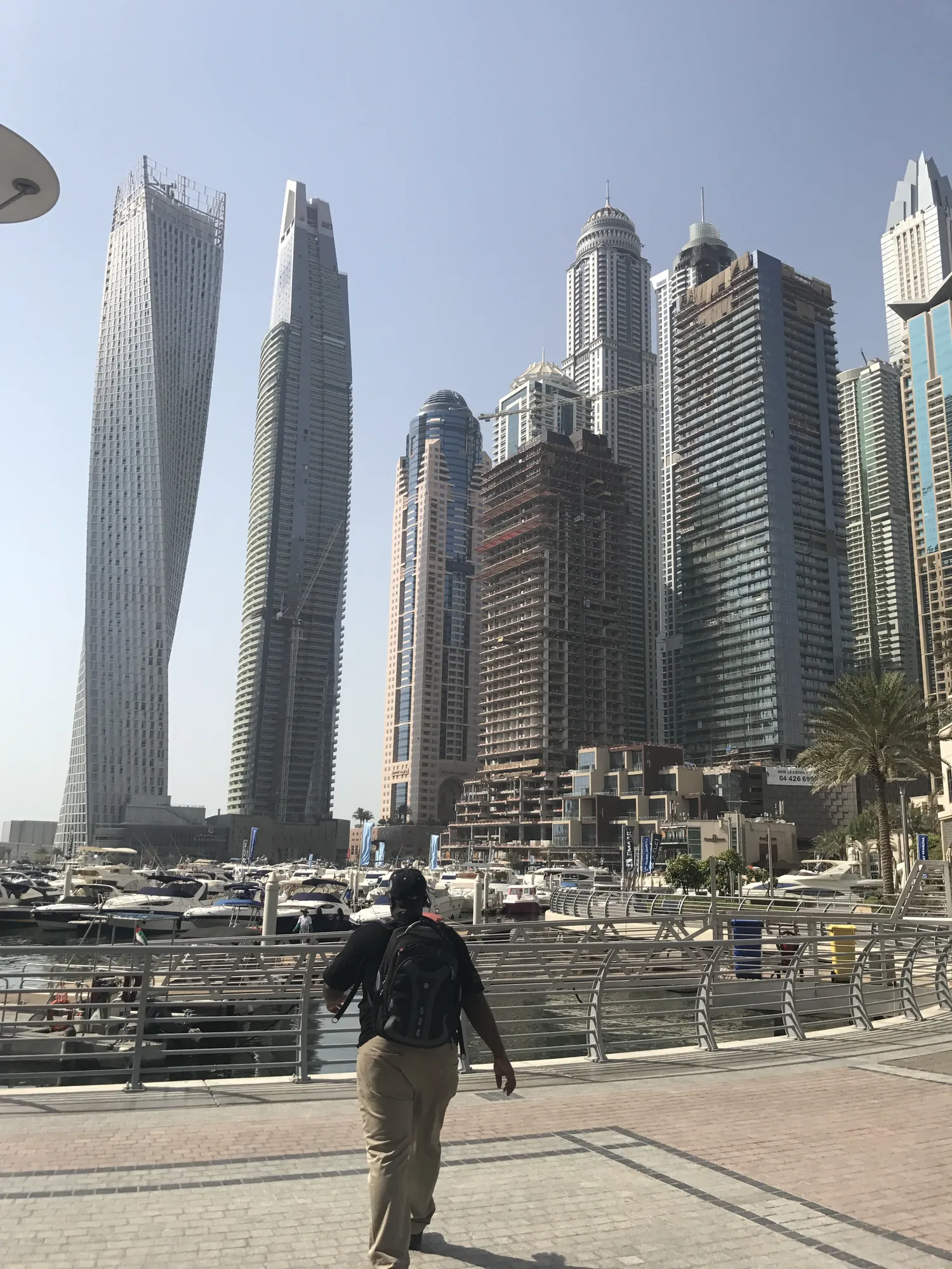Asong walking along Dubai Marina beneath the twisting Cayan Tower