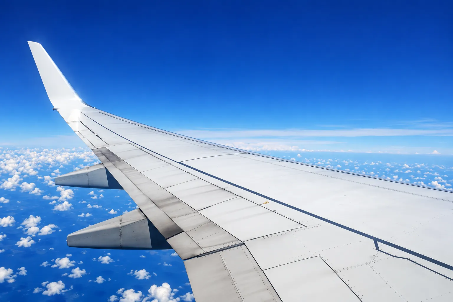 An airliner wing over bright clouds and deep blue sky