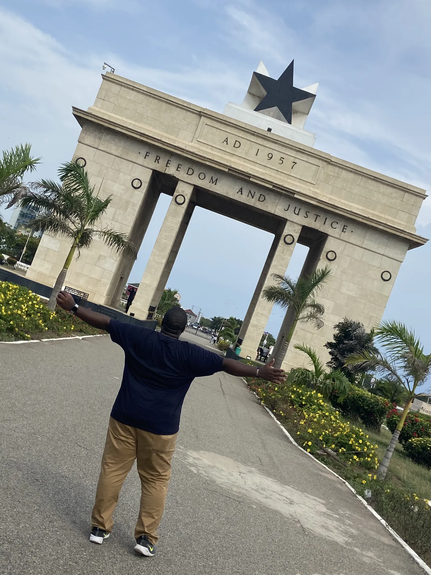 Asong with arms open beneath the Independence Arch and Black Star in Accra