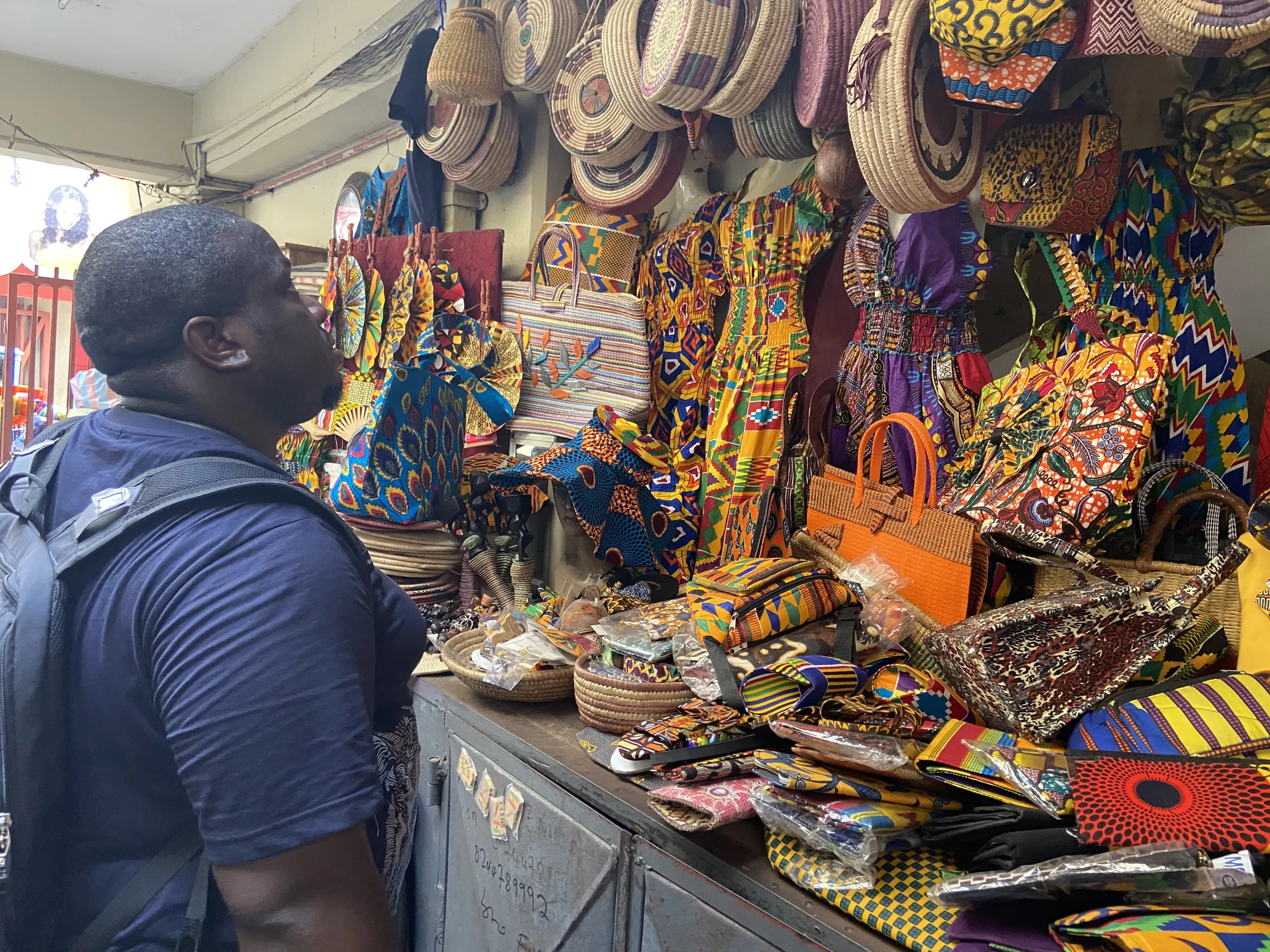 Asong browsing kente cloth, bags and woven hats at a Ghana craft market