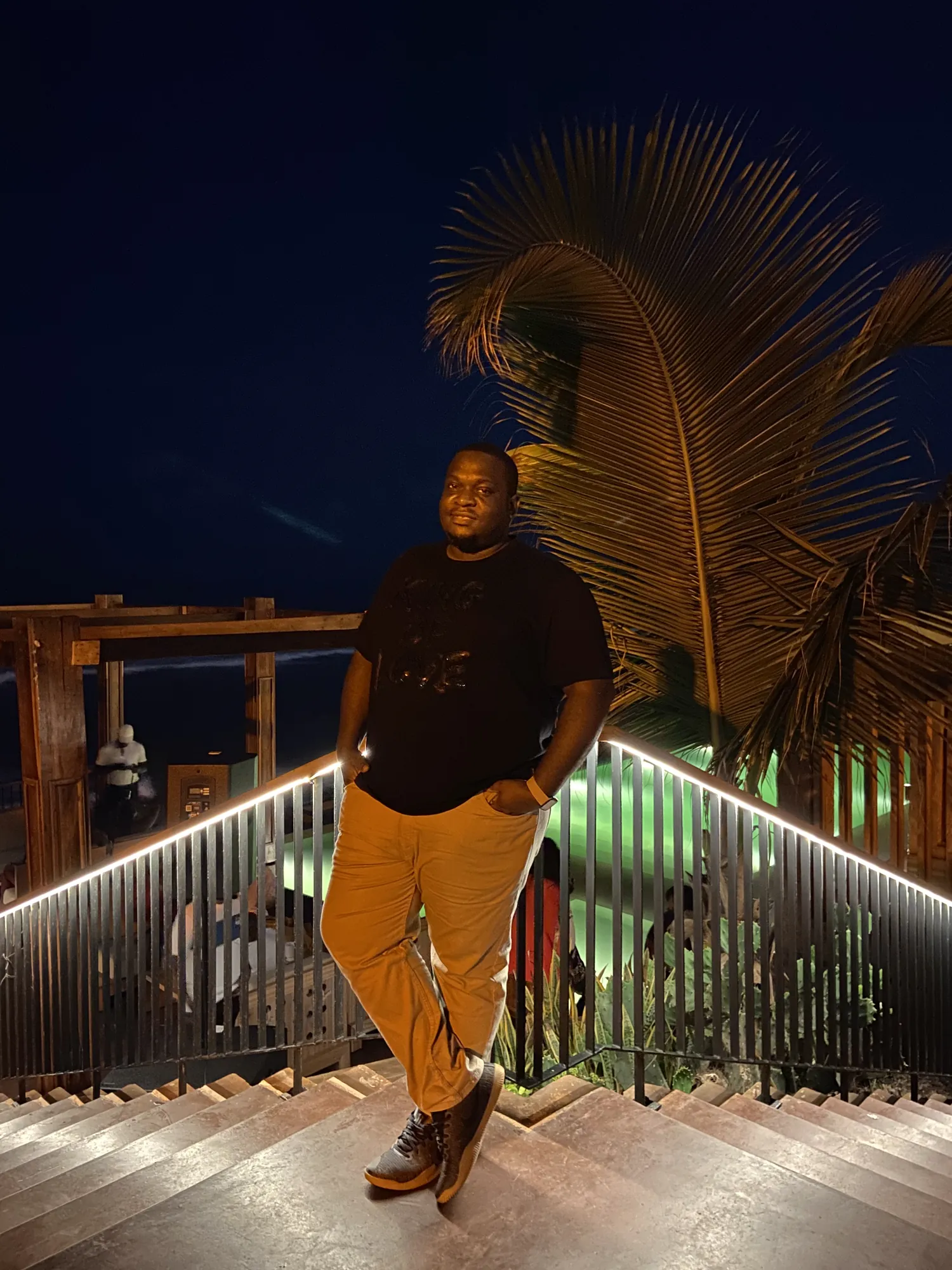 Asong on a lit timber deck under palm fronds at night in Ghana
